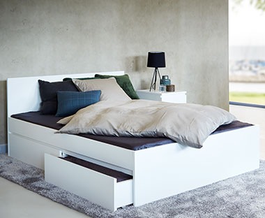 Białe łóżko z wysuwaną szufladą na szarym, miękkim dywanie 