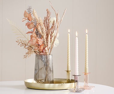 Dekoracja z kręconych świeczek, wazonu ze sztucznymi kwiatami oraz złotej tacy 
