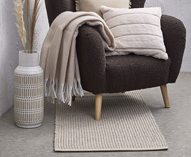 Ciemny fotel z jasnym kocem, poduszką i dywanem 
