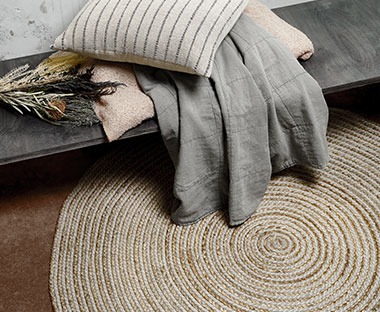 Okrągły, pleciony dywan i kompozycja z koców i poduszek