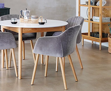 Okragły stół z białym blatem i drewnianymi nogami oraz tapicerowane, wygodne, szare krzesła 