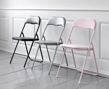 Trzy kolorowe krzesła rozkładane na tle białej ściany 