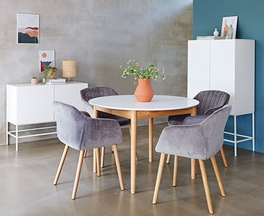 Okrągły stół z białym blatem i drewnianymi nogami oraz szare, tapicerowane krzesła 
