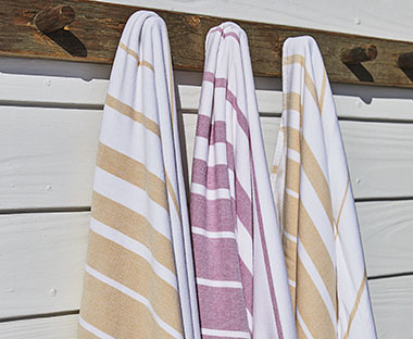 Trzy ręczniki w żółte i różowe paski wiszące na hakach