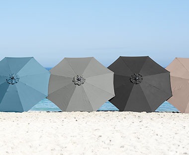 Cztery parasole ogrodowe ułożone na piasku 