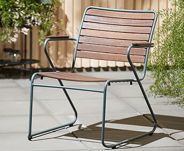Niskie krzesło wypoczynkowe z zielonymi elementami metalowymi i drewnianym siedziskiem i oparciem. 