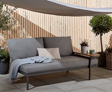 Zgrabna sofa ogrodowa z szarymi poduszkami na ciemnych, stalowych nogach 