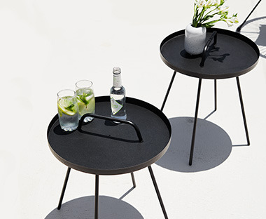 Dwa czarne, okrągłe, metalowe stoliki ze świeżymi ziołami 