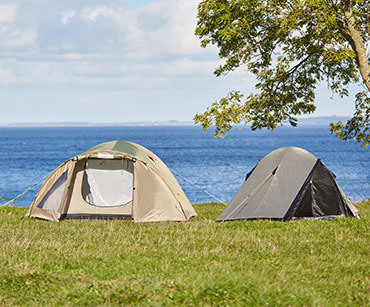 Dwa namioty rozłożone na trawie nad brzegiem wodu 