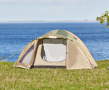 Jasny namiot rozłożony na trawie nad brzegiem wody 
