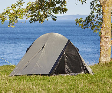 Namiot rozłożony na trawie nad brzegiem jeziora 