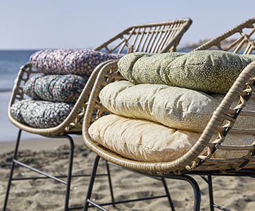 Dwa krzesła na plaży na których leżą po 3 poduszki. 