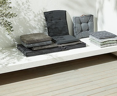 Ciemne, kwadratowe poduszki siedziska ułożone na białej ławce
