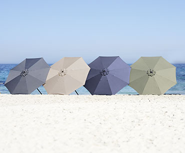 Cztery rozłożone parasole na plaży w kolorze szarym, jasnym, granatowym i oliwkowym 