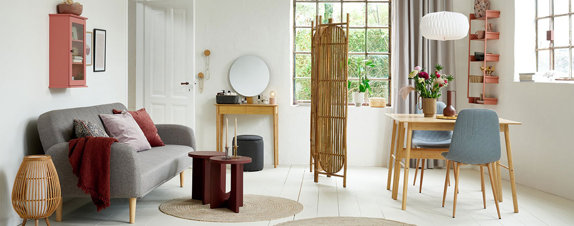Salon i jadalnia z różową półką ścienną, szarą rozkładaną sofą, bambusowym parawanem, bambusowymi biurkami i szarymi krzesłami do jadalni