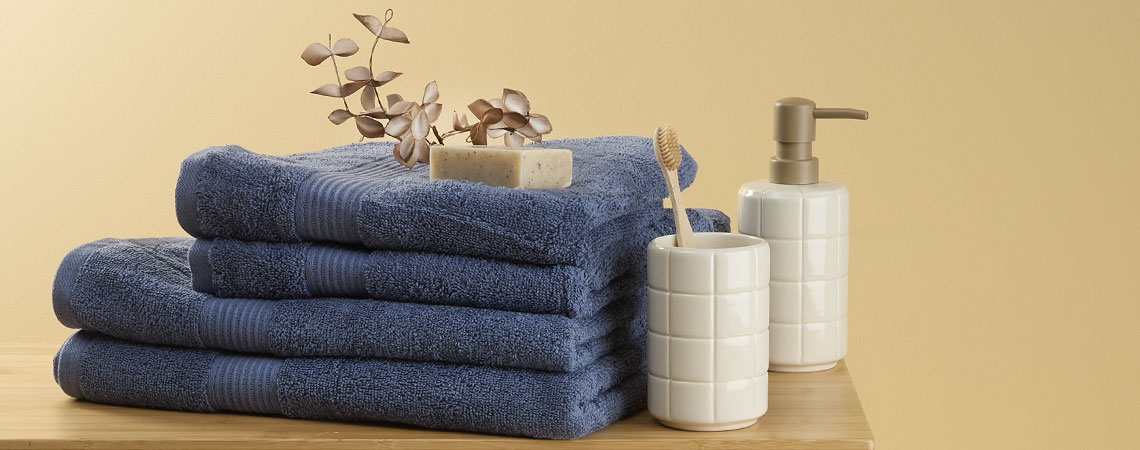 Stos niebieskich ręczników na ławce z uchwytem na szczoteczkę do zębów i dozownikiem mydła 