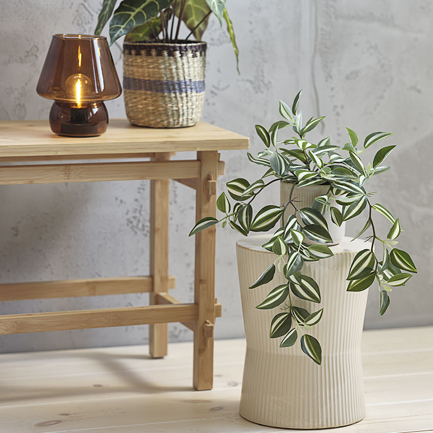 Sztuczna roślina w doniczce na białym żebrowanym stoliku ozdobnym