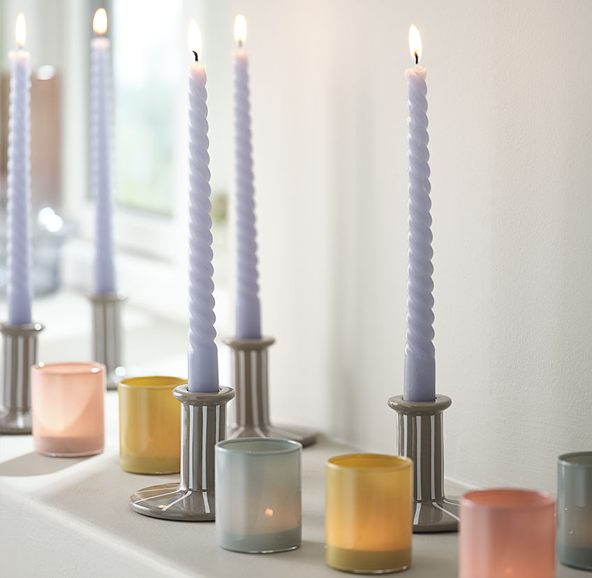 Jasnoniebieska zakręcona świeca w świeczniku z białymi paskami oraz świeczniki na świeczki typu tealight w kolorze niebieskim, żółtym i czerwonym