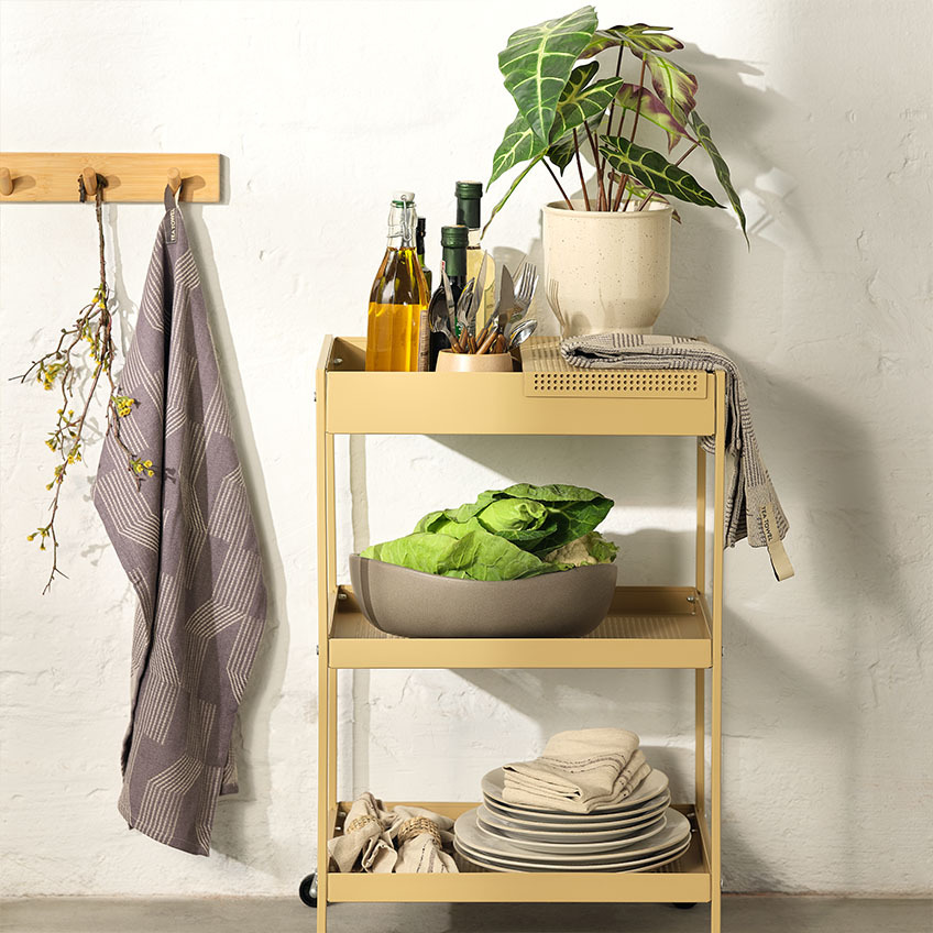 Zastawa stołowa na wózku w kuchni z talerzami obiadowymi, dużą miską, zestawem sztućców i sztuczną rośliną