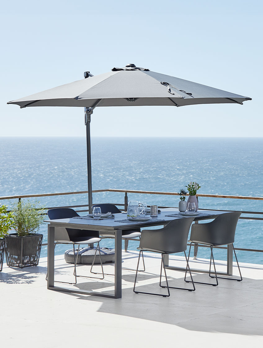 Duży wiszący parasol oraz stół i krzesła ogrodowe na tarasie z widokiem na ocean