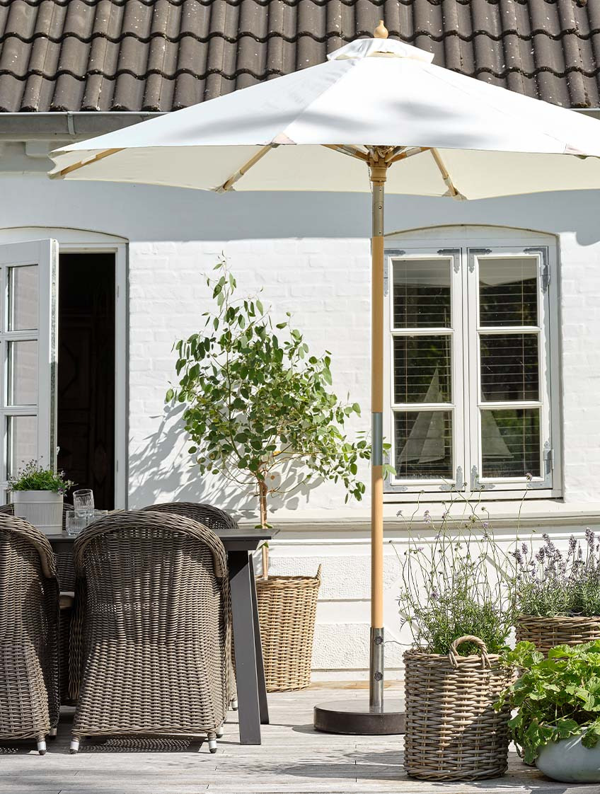 Klasyczny parasol ogrodowy w kolorze naturalnej bieli na tarasie ze stołem ogrodowym i krzesłami ogrodowymi