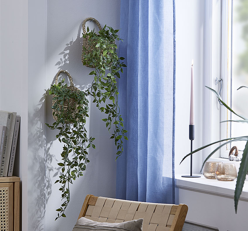 Dwa kosze ze sztucznymi roślinami wiszące na ścianie w salonie
