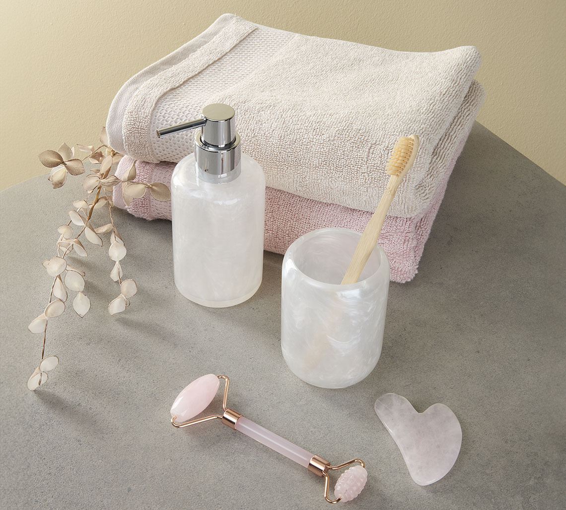 Piaskowy i różowy ręcznik obok stojaka na szczoteczkę do zębów, dozownika mydła i wałka do twarzy 