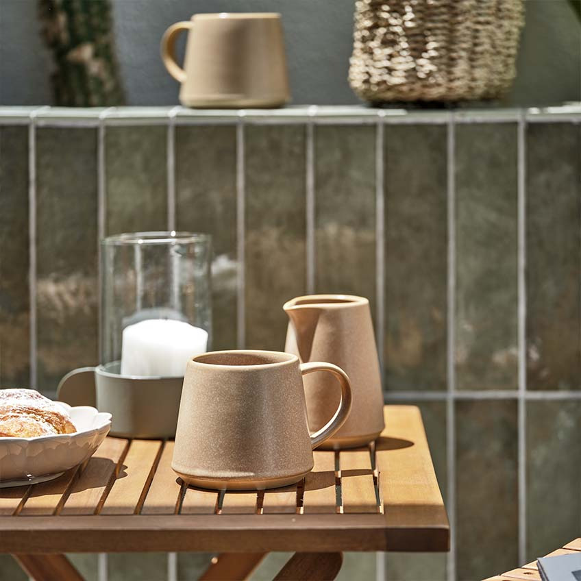 Kubek z kawą i słoik z mlekiem na małym drewnianym stoliku ogrodowym w pełnym słońcu 