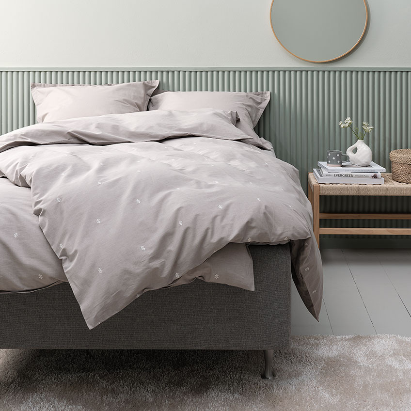 Zestaw jasnoszarej kołdry i bawełnianej pościeli wraz z poszewką na poduszkę na łóżku w sypialni