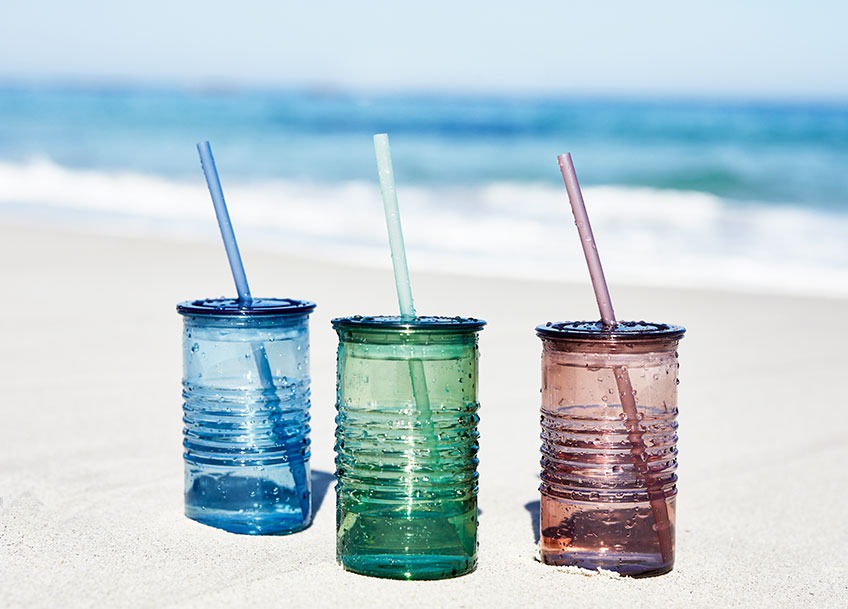Three drinking cups in different colours in the sand on a beach 