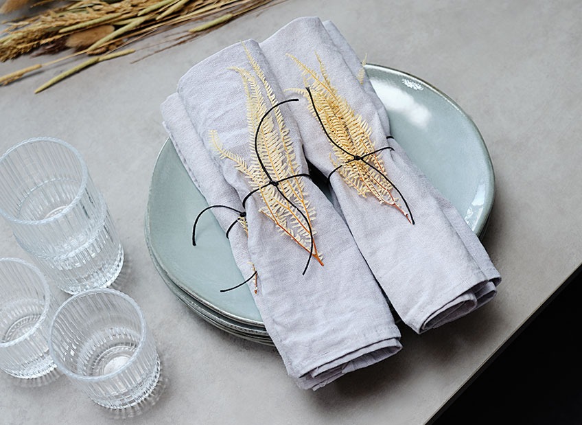 Zestaw stołowy z talerzem, szklankami i serwetkami ozdobionymi suszonymi liśćmi i wstążką