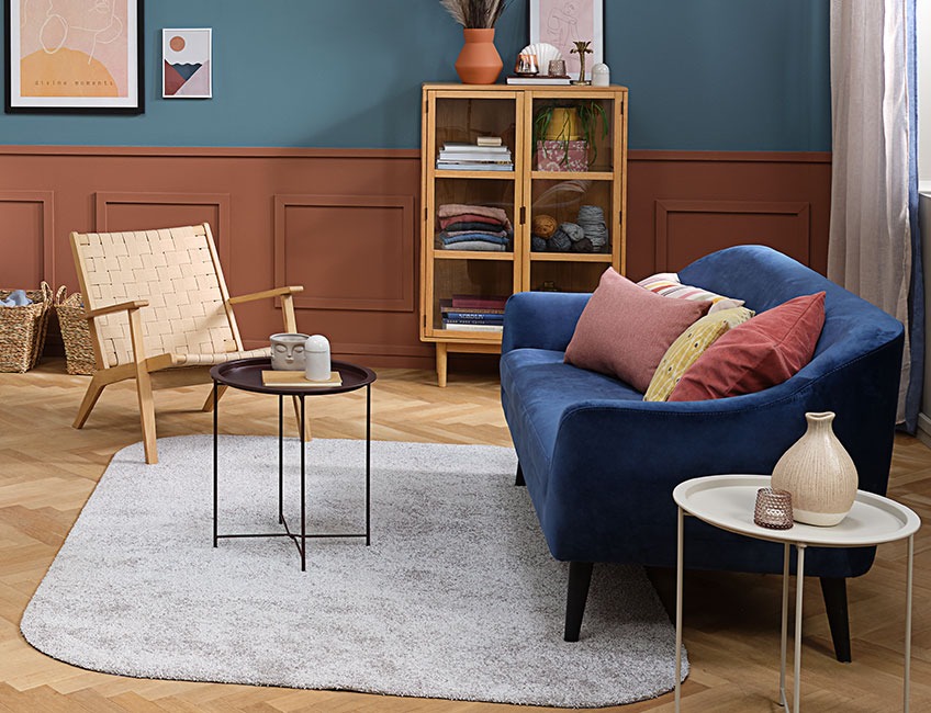 Salon z jasnoszarym dywanikiem, fotelem i sofą z kolorowymi poduszkami