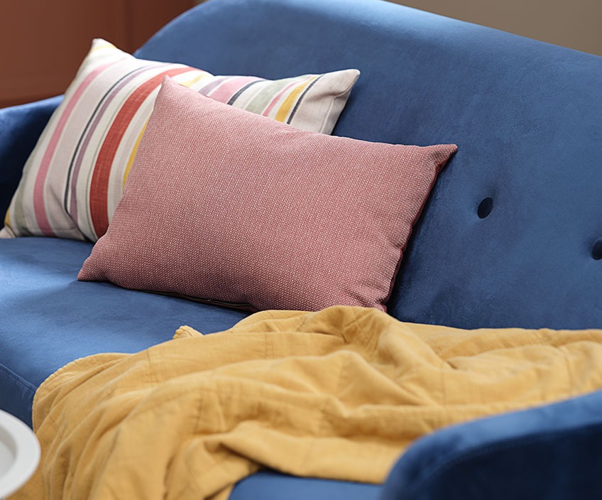 Kolorowe poduszki i pikowany koc na niebieskiej sofie