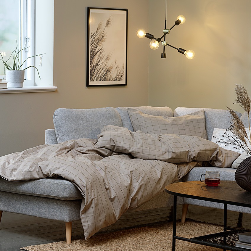 sofa AARHUS, kołdra w zestawie poszewek TANJA i zawieszka TORSTEIN Salon „hygge” z dużym narożnikiem, kołdrą i oświetleniem