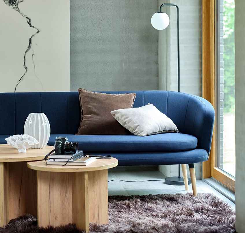 Niebieska sofa, okrągłe stoliki kawowe, brązowy dywan i lampa podłogowa