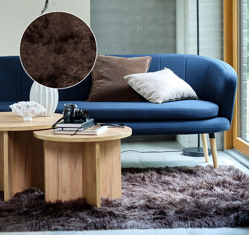 Salon z brązowym dywanikiem ze sztucznego futra, niebieską sofą i okrągłymi stolikami kawowymi