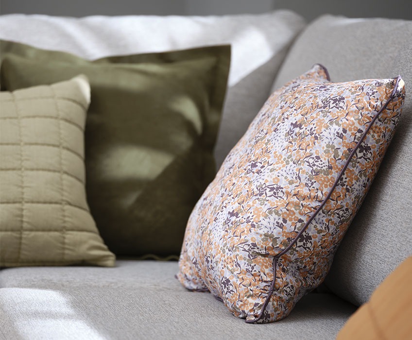 Szafa kanapa z poduszkami w odcieniach zieleni i w poszewce z kwiatkami 