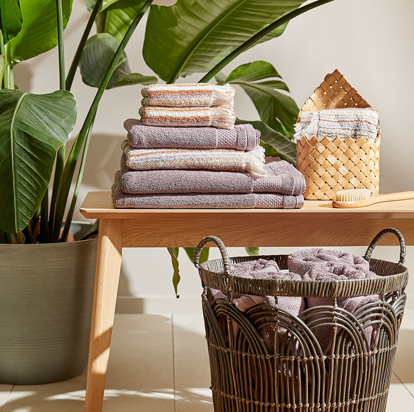 Ręczniki bawełniane i wiklinowy kosz na ławce w łazience