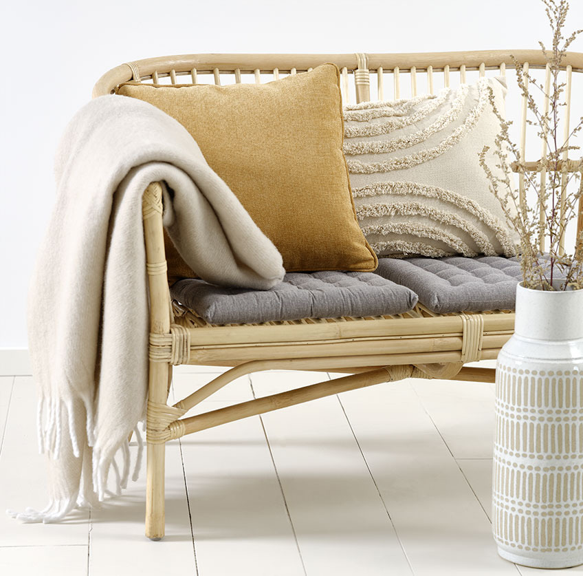 Sofa LISELEJE, beżowa poduszka GRAVMYRT, żółtka poduszka HORNFIOL i koc TUSENFYRD Rattanowa sofa z beżową i żółtą poduszką oraz beżowym kocem