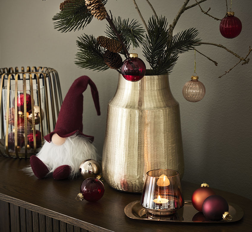 złoty świecznik, świąteczny elf, i złoty wazon ze świerkowymi gałązkami i bombkami. 