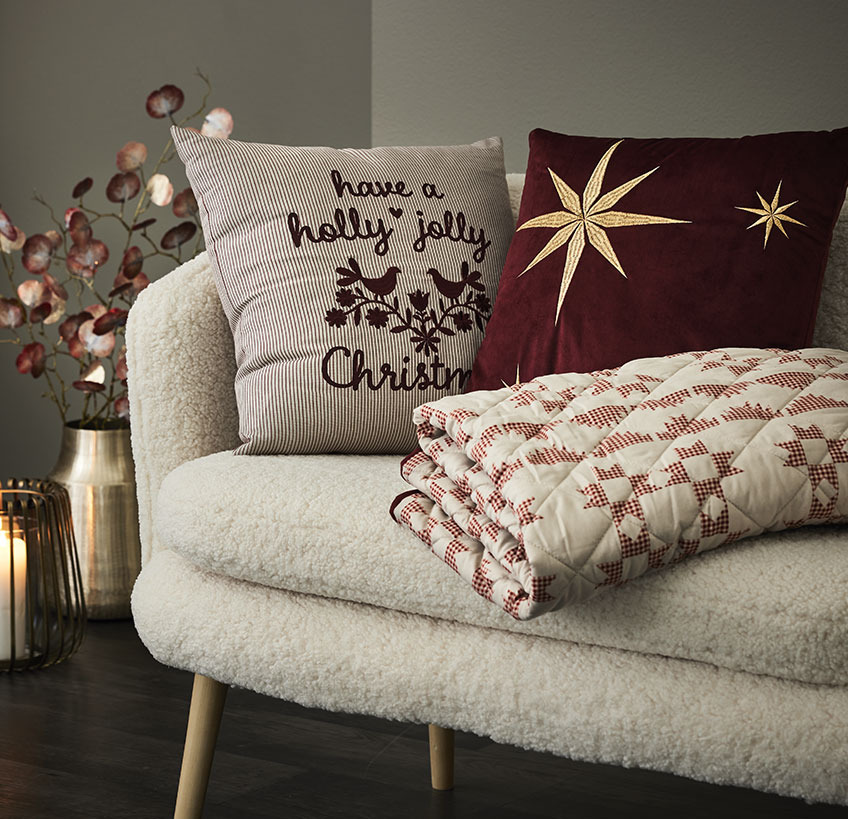 Poduszki i pikowany koc ze świątecznymi wzorami na białej sofie 