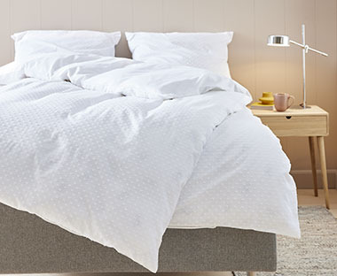 Dwuosobowe łóżku z kołdrą i dwoma poduszkami w białej pościeli 