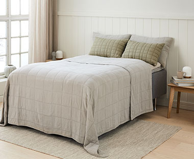Sypialnia z łóżkiem, na którym leży szara narzuta i oliwkozielone poduszki ozdobne